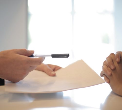 The hands of a person giving pen and papers to another