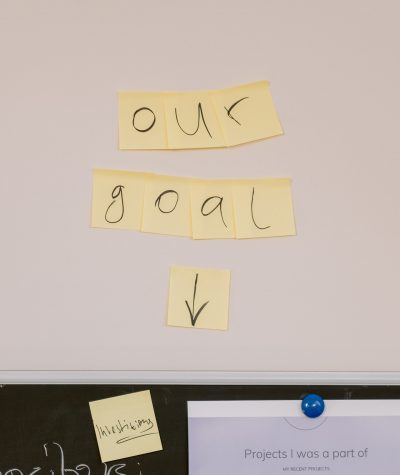 A sign made of letters written on sticky notes saying "our goal" and an arrow pointing to a black board